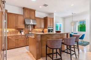 A modern kitchen with wooden cabinets, a stainless steel range hood, and a central island with bar stools. - Luxury Estate Home in Andreas Hills All En Suite, Saltwater Pool & Spa, Fire Pit (Palm Springs)