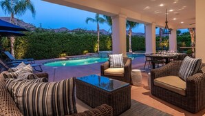 An outdoor patio area with a pool, wicker furniture, and a dining table set for a meal. - Luxury Estate Home in Andreas Hills All En Suite, Saltwater Pool & Spa, Fire Pit (Palm Springs)