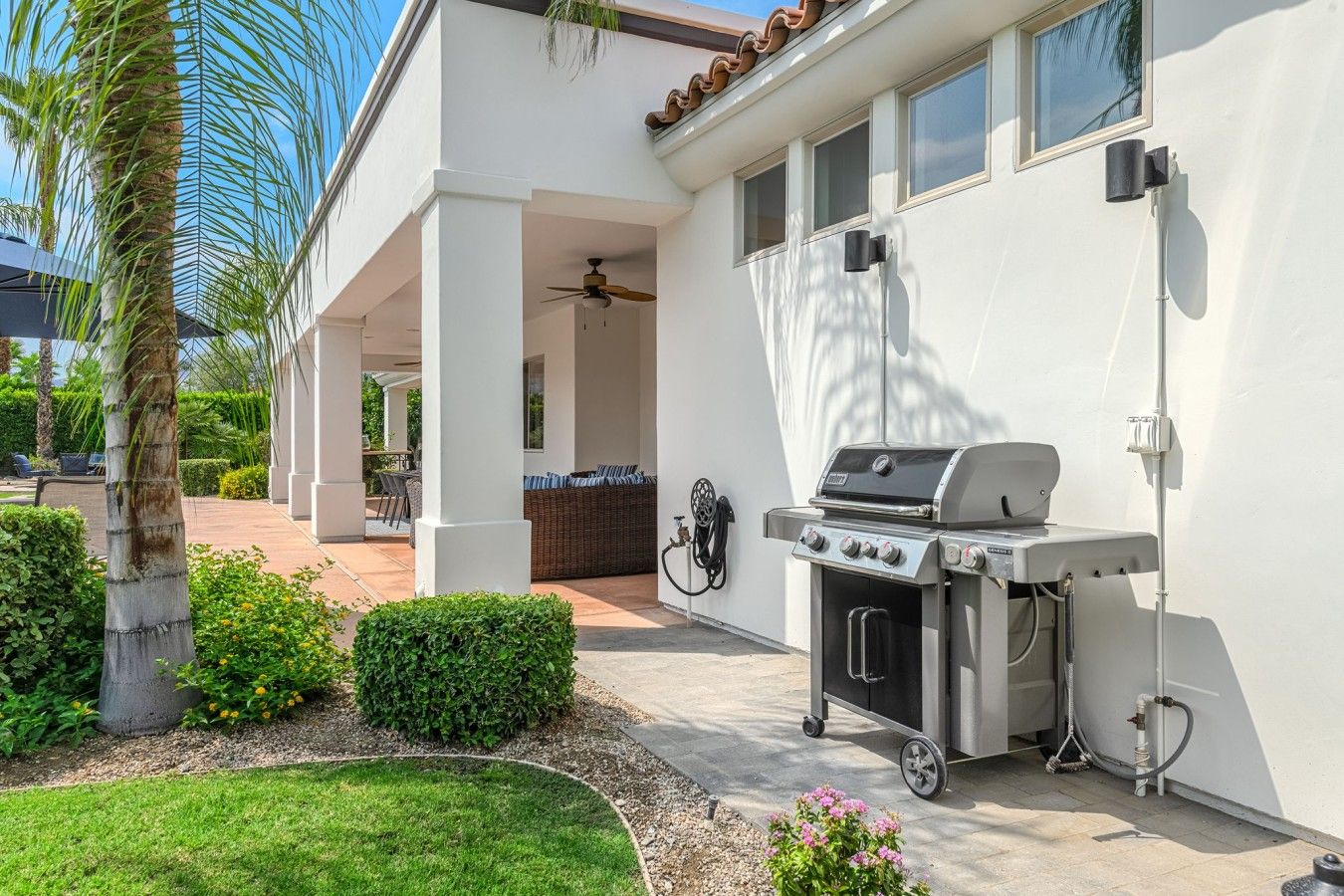 A patio with a grill, a covered seating area, and a view of a house.