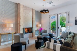 A modern living room with a fireplace, patterned wallpaper, and a view through glass doors.