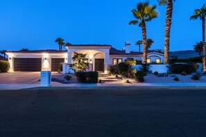 A two-story house with a garage, a covered patio, and palm trees.