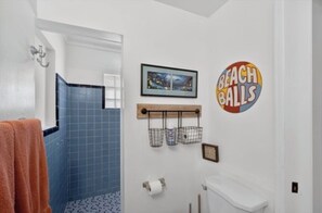 Een badkamer met een blauw betegelde douche, toilet, wastafel en een handdoekhouder met een strandthema-wanddecoratie.