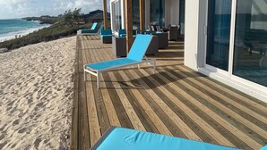 A wooden deck with blue lounge chairs and a glass door leading to a room.