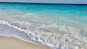 A beach with clear turquoise water and foamy waves.