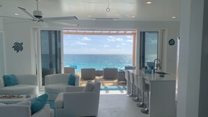 A modern living room with a view of the ocean, a ceiling fan, and a bar area.