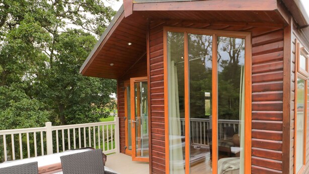 A wooden cabin with a deck, outdoor seating, and a glass door leading to a patio area. - Number 43 Burnside Lodge (Morpeth)