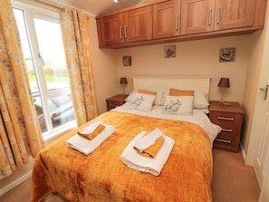 Quarto de hotel com cama, armários de madeira, mesa de cabeceira e janela com cortinas.