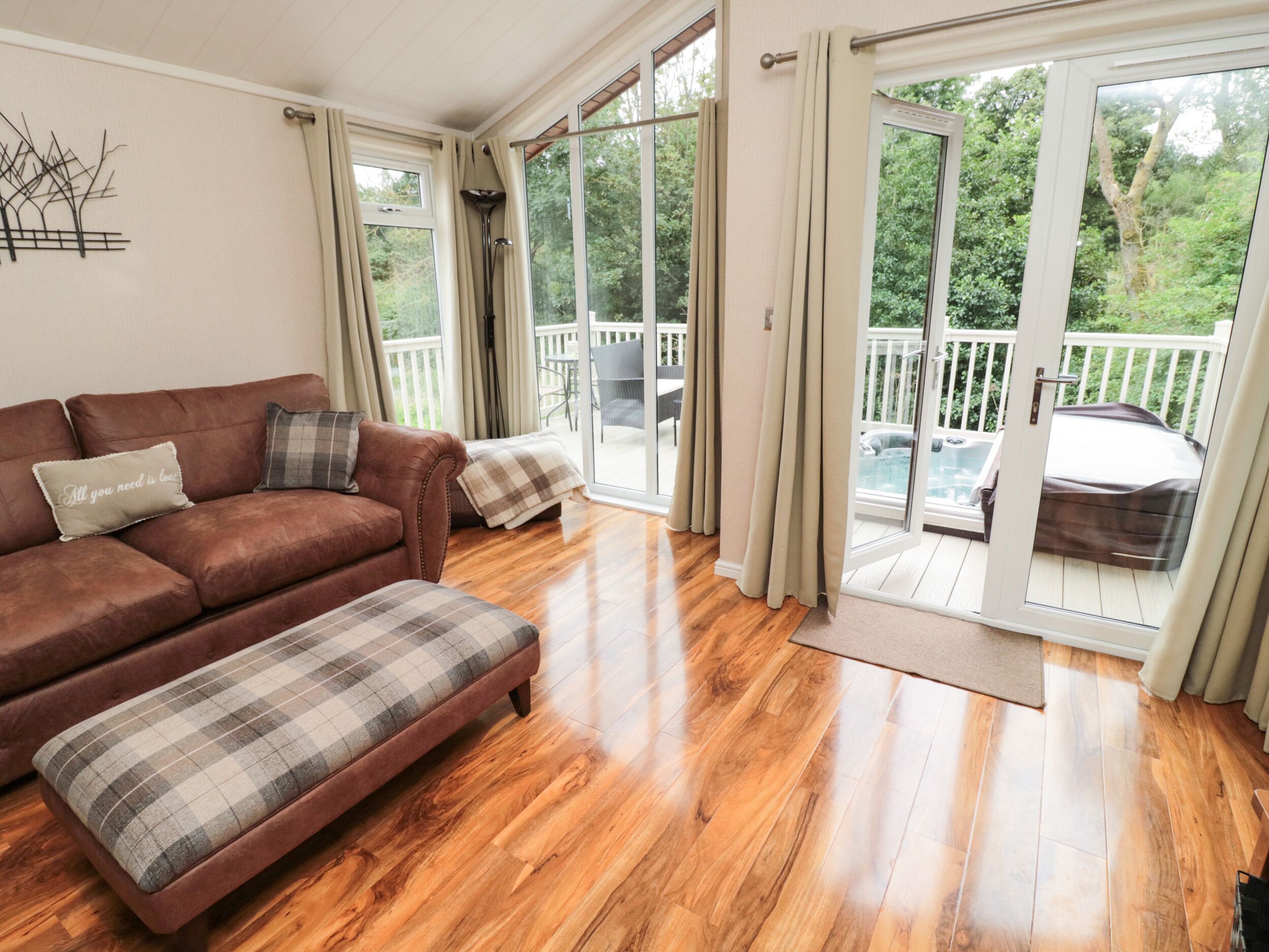 Een ruime woonkamer met een bruine leren bank, een gestreept voetenbankje en uitzicht op een houten terras en jacuzzi door grote schuifdeuren van glas.