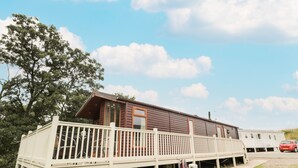 A wooden cabin with a deck, a large window, and a door. - Number 43 Burnside Lodge (Morpeth)