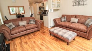 A living room with two brown leather sofas, a wooden floor, and a kitchen in the background. - Number 43 Burnside Lodge (Morpeth)