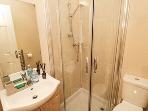 Casa de banho com cabine de duche em vidro, lavatório com artigos de higiene e sanita.
