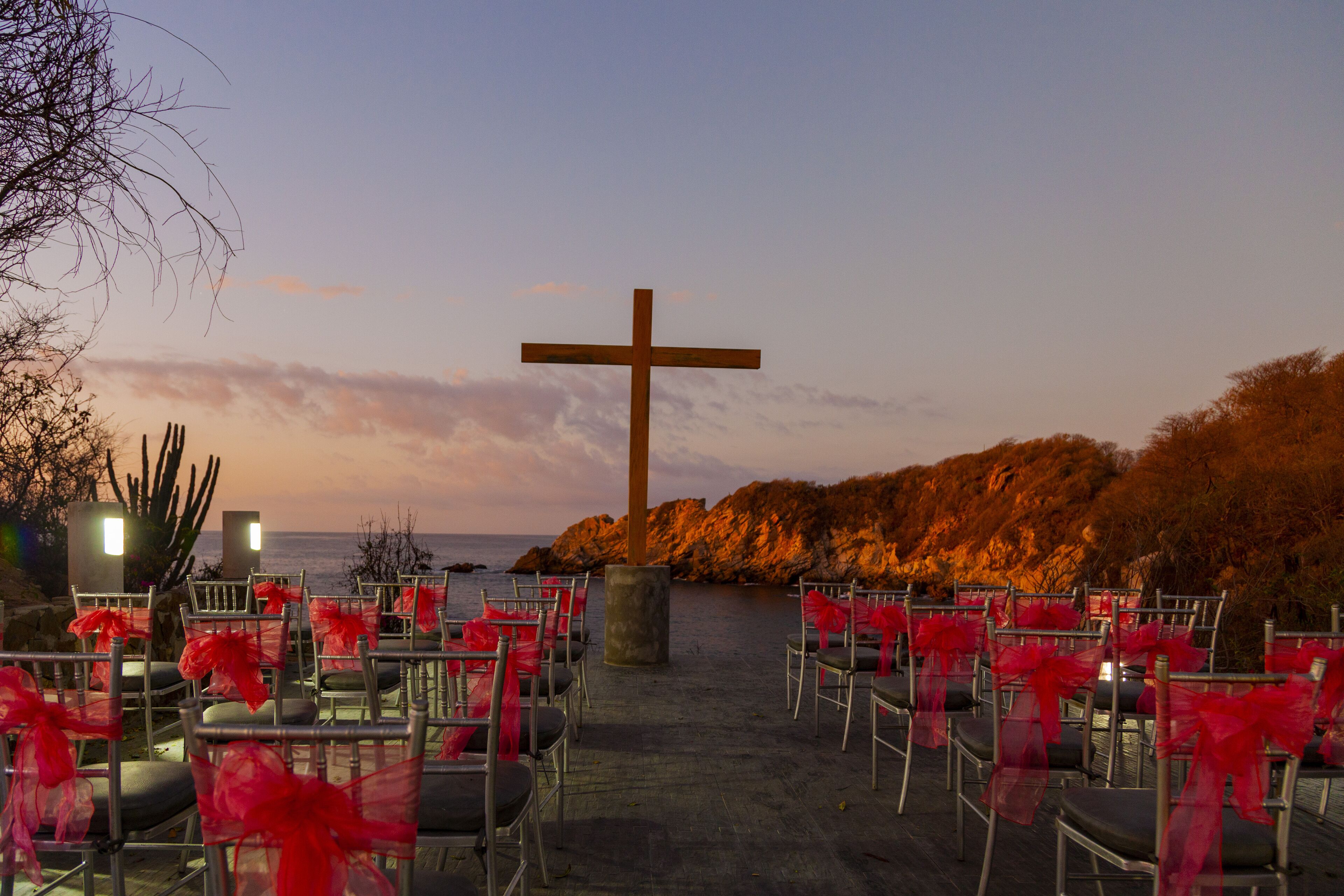 A church with pews arranged in rows, a large wooden cross, and a view of the sea.