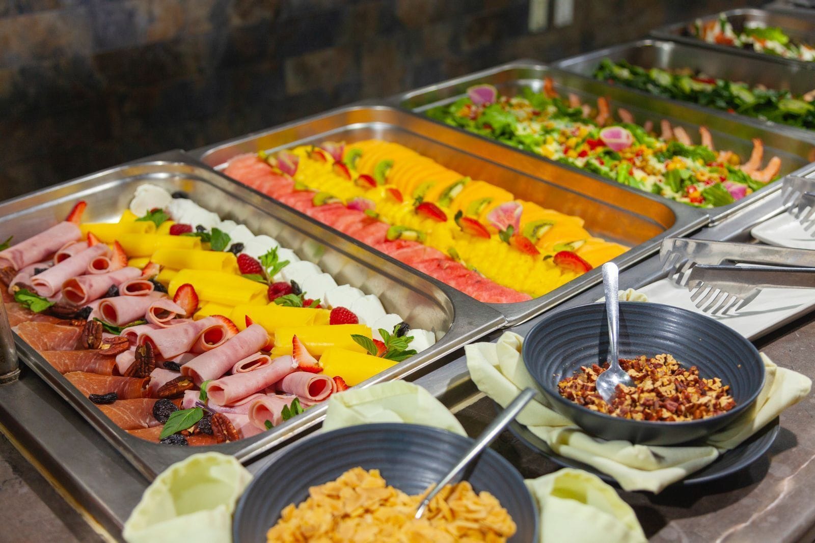 A buffet with various food options including meats, fruits, and salads.