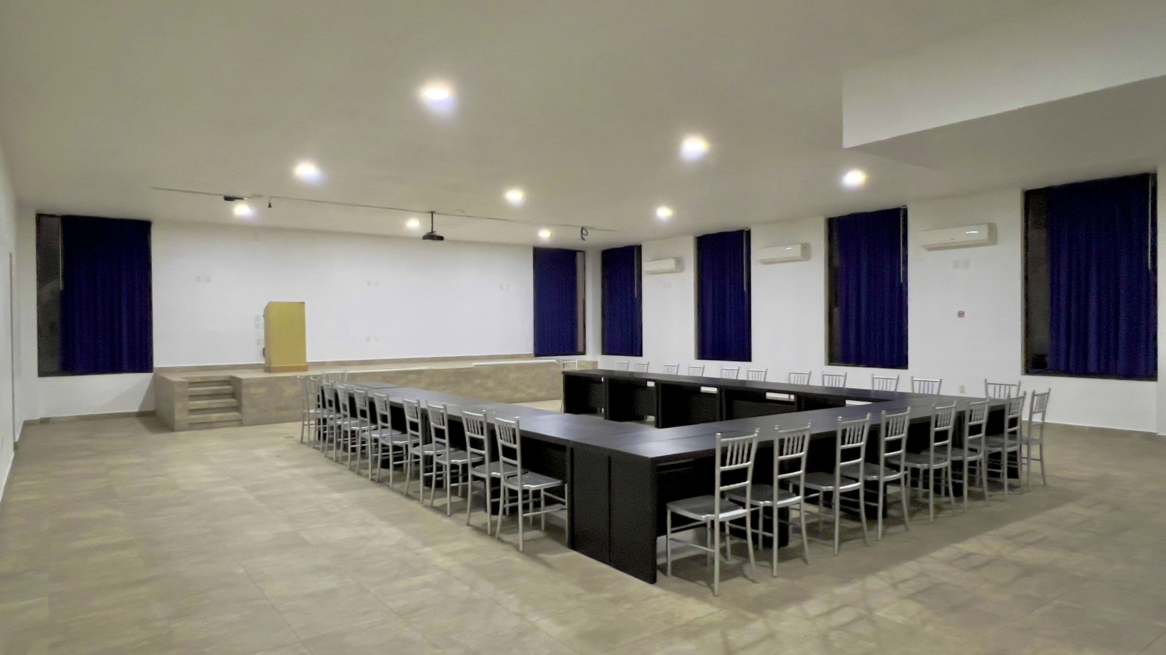 A conference room with a long table and chairs, white walls, and blue curtains.