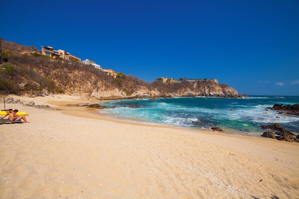 A beach with a rocky cliff and buildings on top. - Coral Blue Huatulco All Inclusive (Santa María Huatulco)