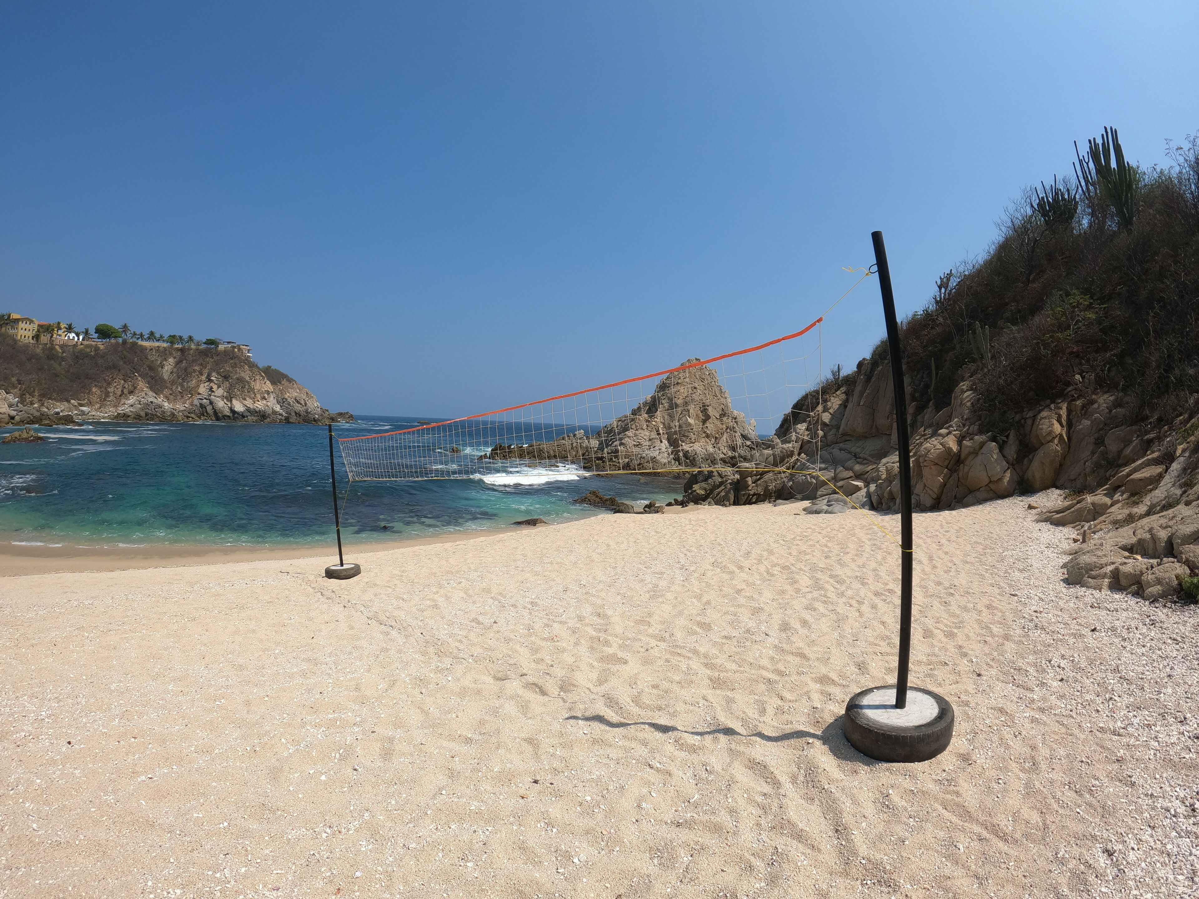 A sandy beach with a volleyball net and a rocky cliff in the background.