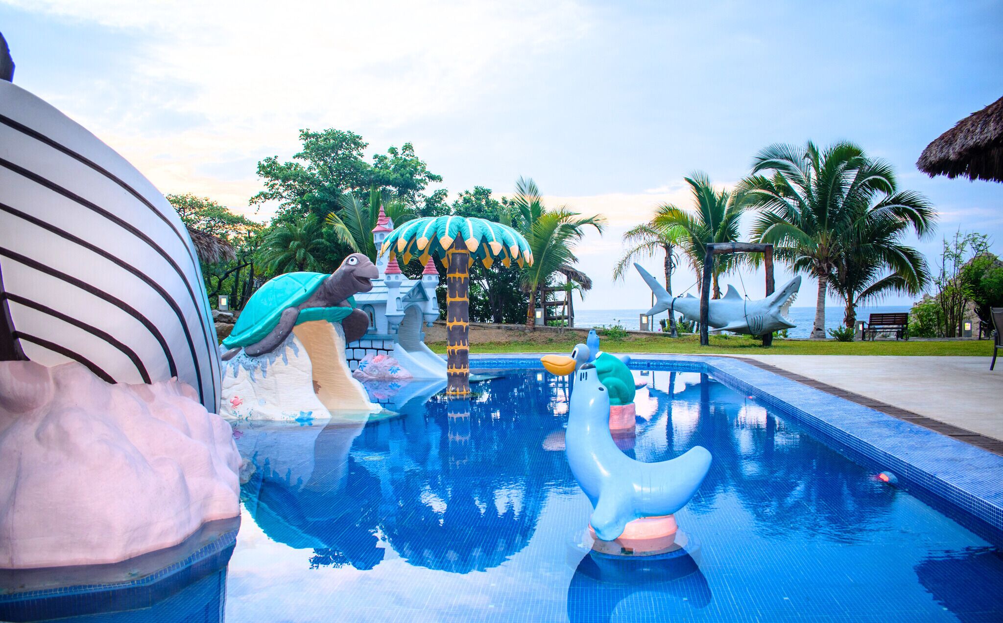 Una piscina con tobogán, una escultura de tortuga y una escultura de tiburón.