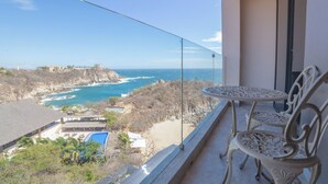 Ein Balkon mit Tisch und Stühlen mit Blick auf eine Küstenlandschaft, inklusive Pool und Gebäuden in der Ferne.