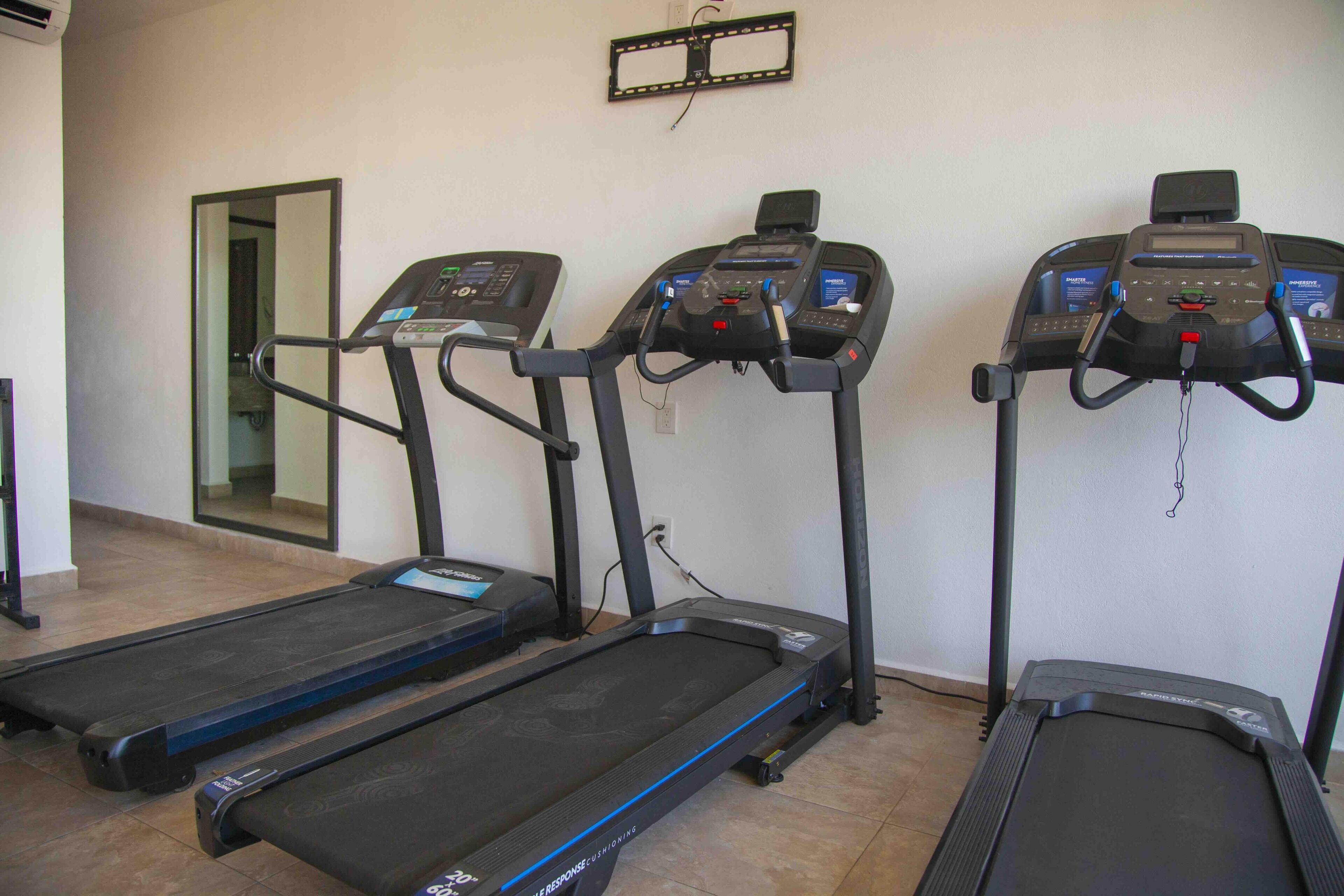 Tres cintas de correr en una sala con suelo de baldosas y una puerta al fondo.