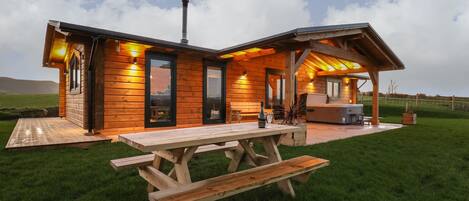 A wooden cabin with a covered patio, a barbecue area, and a picnic table.