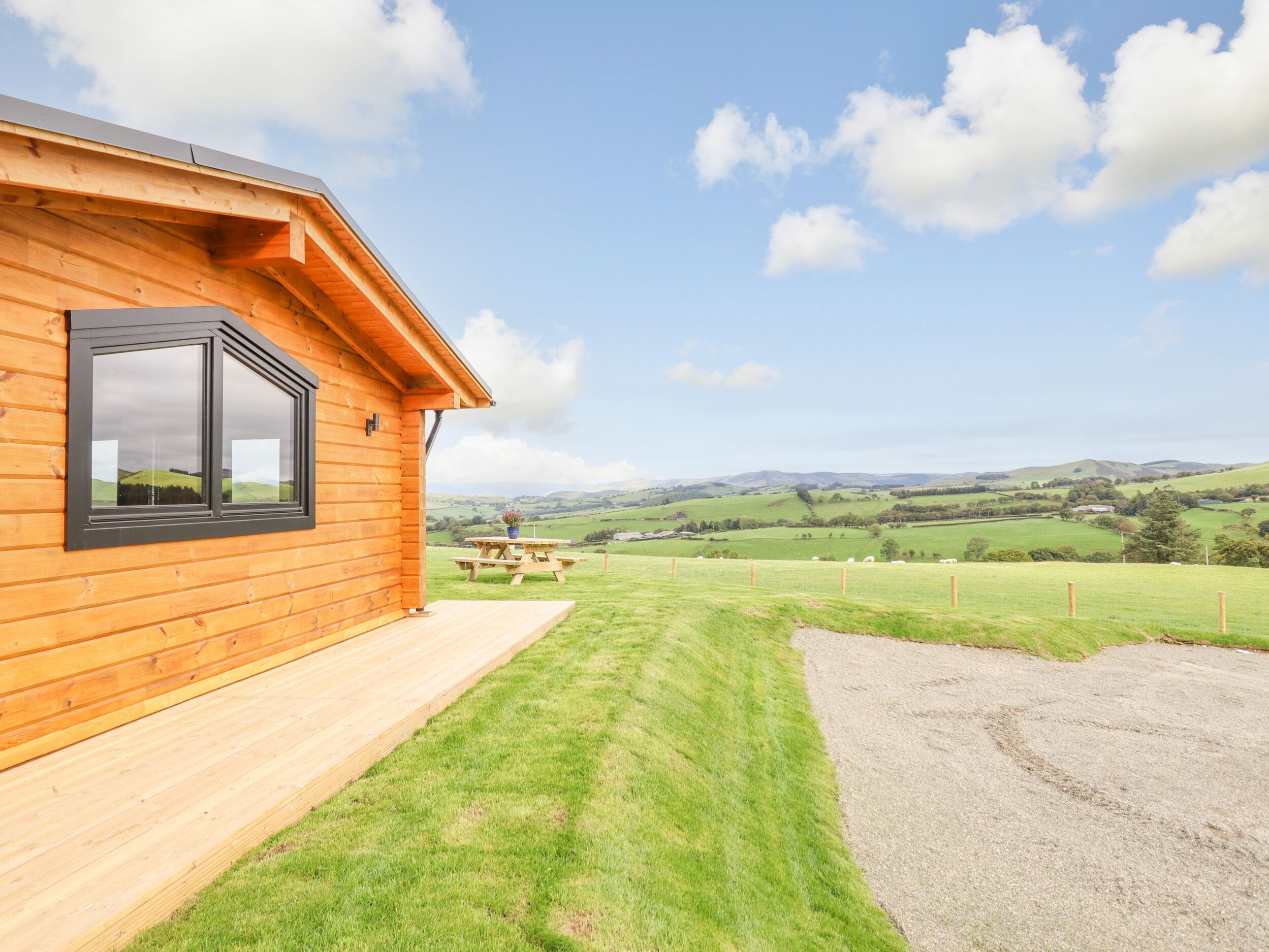A wooden cabin with a large window, a picnic table, and a grassy yard.