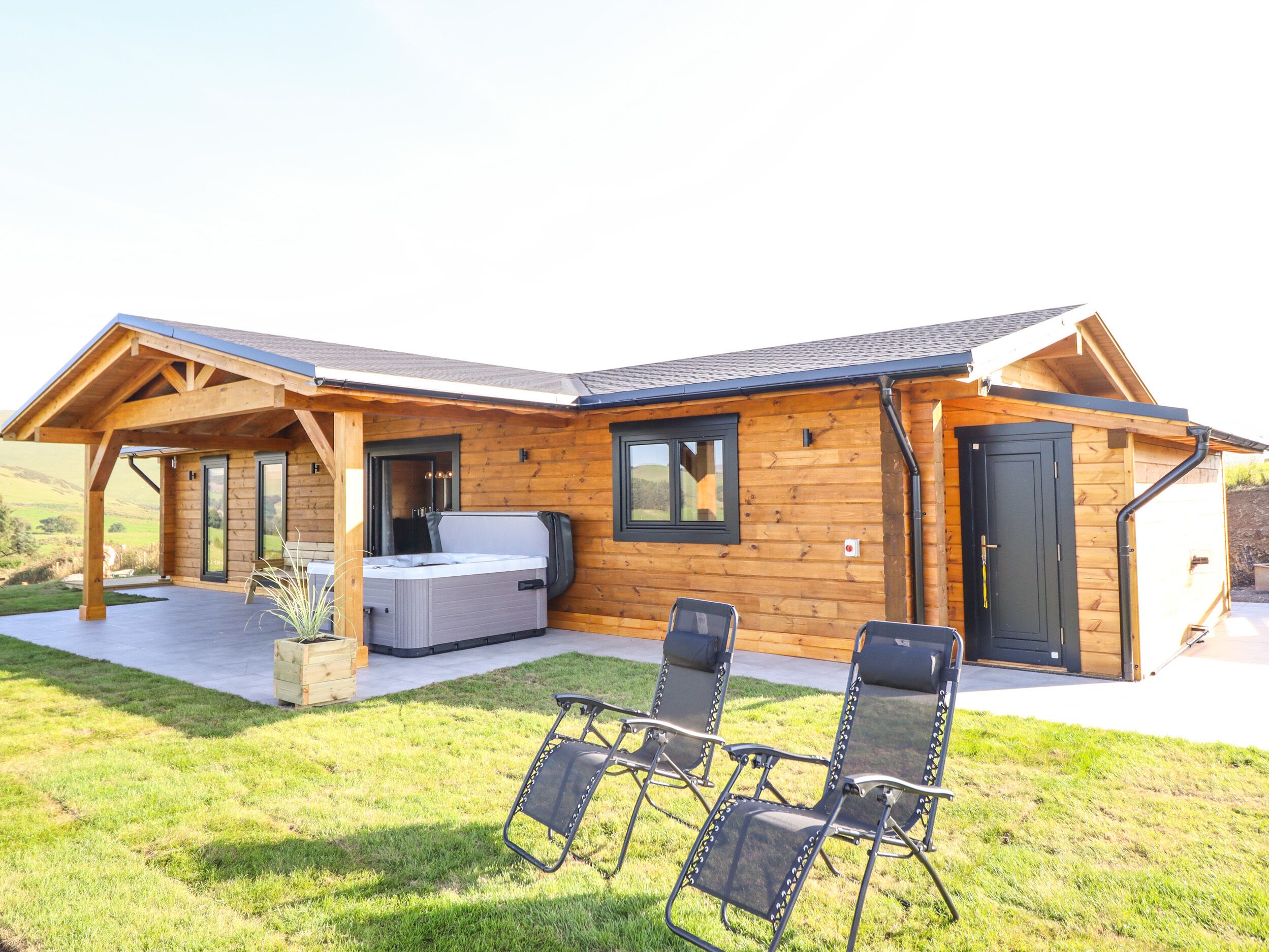 A wooden cabin with a hot tub, outdoor seating, and a covered patio.