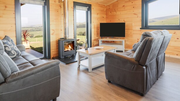 A cozy living room with a wood-burning stove, a flat-screen TV, and comfortable seating. - Bacheiddon Log Cabin (Machynlleth)