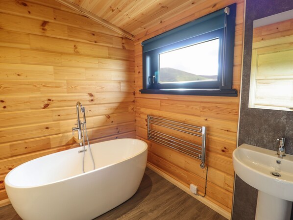 A wooden cabin bathroom with a freestanding bathtub, a window, and a sink.