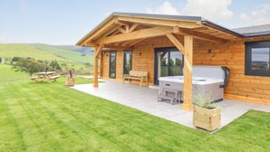 A wooden cabin with a covered patio, a barbecue grill, and a picnic table. - Bacheiddon Log Cabin (Machynlleth)
