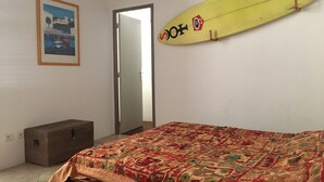 A bedroom with a bed, a wall-mounted surfboard, a door, and a framed picture.