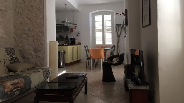 A living room with a sofa, a coffee table, and a TV stand. There is a kitchen area with a dining table and chairs.