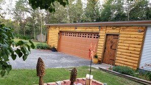 Una baita di legno con un garage e un giardino curato con alberi ornamentali e un abbeveratoio per uccelli.