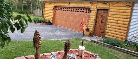 A log cabin with a garage and a well-maintained garden with decorative trees and a bird feeder.