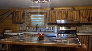 Una cucina con mobili in legno, una grande isola con sgabelli, un lampadario e una finestra con persiane.