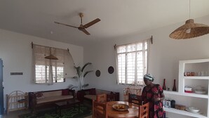 A spacious living area with a dining table, chairs, a sofa, a ceiling fan, and a large window with curtains. - Lovely 4-bed Villa for Rent in Nungwi, Zanzibar (Nungwi)