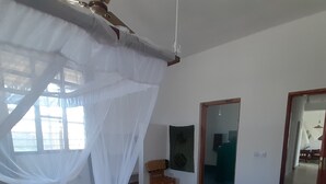 A bedroom with a canopy bed, a wooden floor, a red patterned rug, and a mirror on the wall. - Lovely 4-bed Villa for Rent in Nungwi, Zanzibar (Nungwi)
