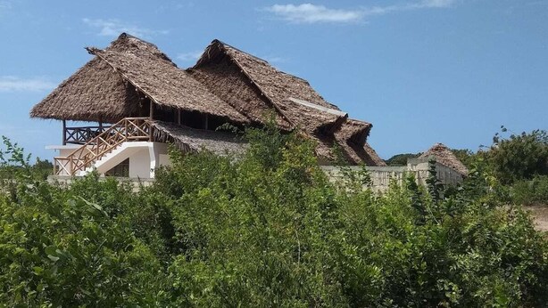 A traditional thatched-roof house with a wooden staircase leading to a balcony. - Lovely 4-bed Villa for Rent in Nungwi, Zanzibar (Nungwi)