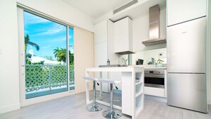 Een moderne keuken met witte kasten, een roestvrijstalen koelkast, een dubbele spoelbak en een grote schuifdeur die leidt naar een balkon met uitzicht op palmbomen.