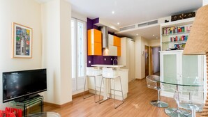 Een moderne woonkamer met een flatscreen televisie, een glazen salontafel en een bar met krukken.
