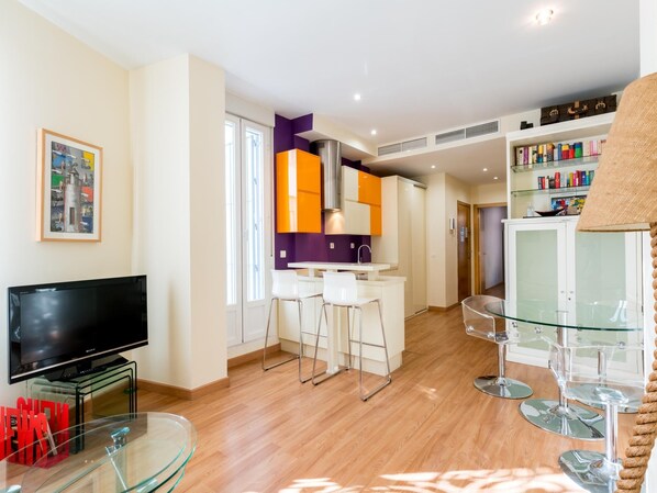 A modern living room with a flat-screen TV, a glass coffee table, and a bar area with stools.