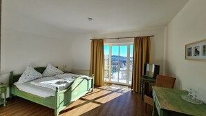 Una stanza con un letto, una televisione, un tavolo con bicchieri e vista su un paesaggio innevato attraverso una finestra.