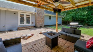 Eine überdachte Terrasse mit Deckenventilator, Sitzgelegenheiten im Freien und Grillbereich.