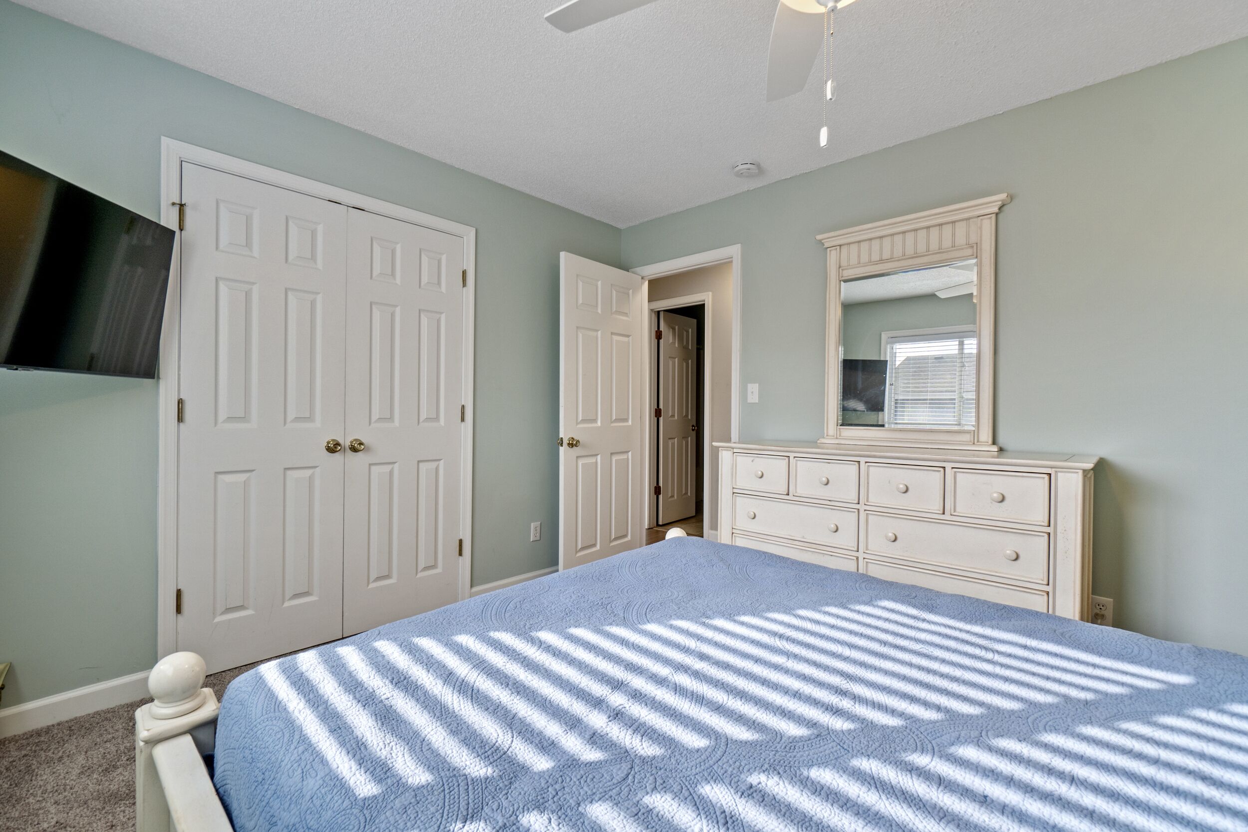 Un dormitorio con cama, cómoda, espejo y dos puertas.