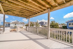 A wooden deck with a white railing, overlooking a residential area with houses and greenery.