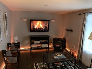 Ein Wohnzimmer mit Kamin, Wandfernseher, Couchtisch mit Büchern und einer Couch.