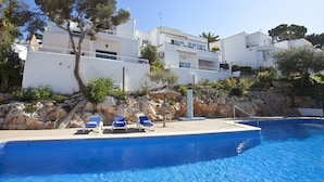 A swimming pool with lounge chairs, white buildings, and trees in the background. - Bungalow Playa D'or, Delante de la Playa con Wifi, A/A y Piscina Comunitaria (Cala D'or)