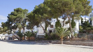 A coastal building with multiple balconies, surrounded by trees and a sandy foreground. - Bungalow Playa D'or, Delante de la Playa con Wifi, A/A y Piscina Comunitaria (Cala D'or)