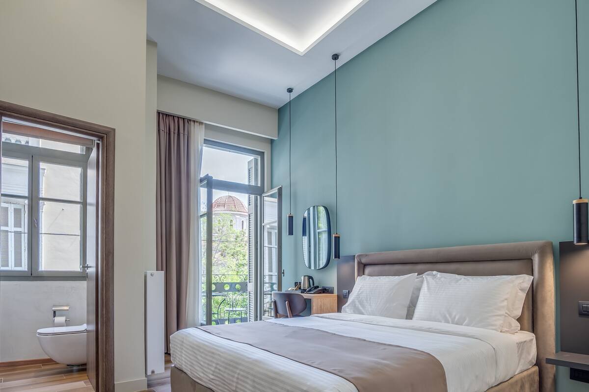 A modern hotel room with a large bed, a desk, and a view of the outdoors.