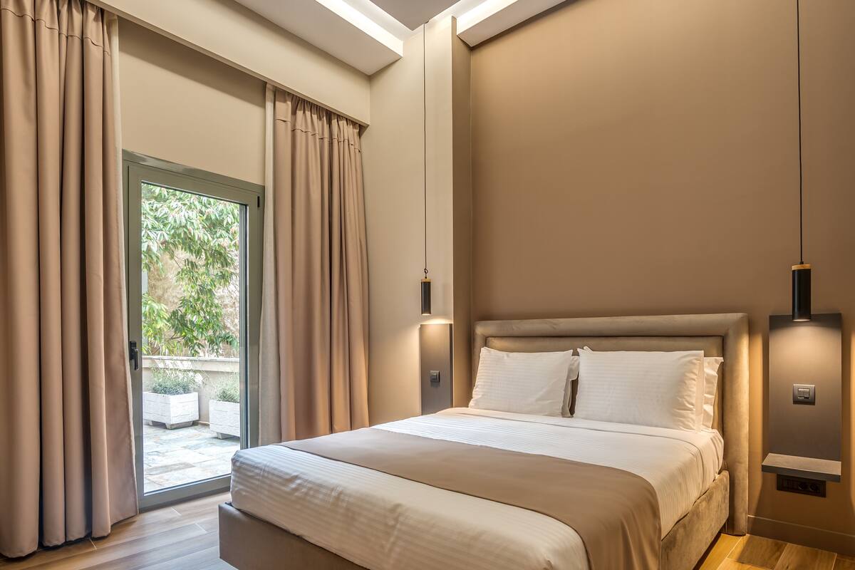 A modern bedroom with a large bed, sliding glass door to a balcony, and ambient wall lighting.