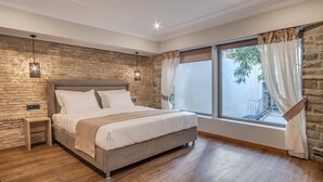 Un dormitorio con una cama grande, pared de piedra, suelo de madera y una ventana con cortinas.